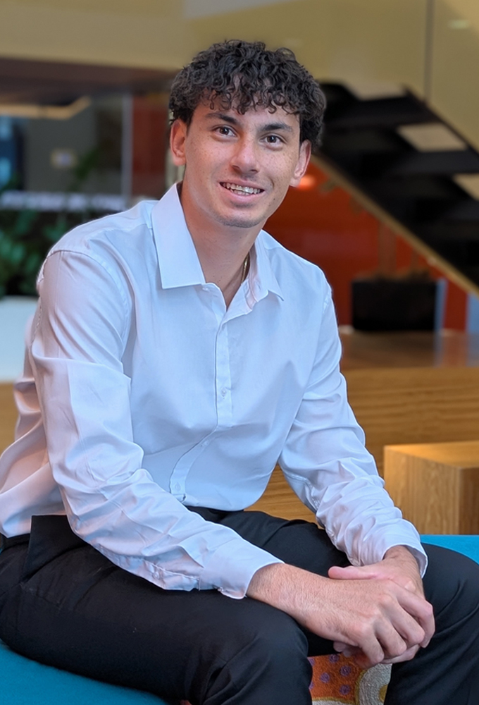 Jack, a young male ATO Evergreen Program graduate, smiling, seated in an ATO workspace, wearing a white shirt and black trousers.