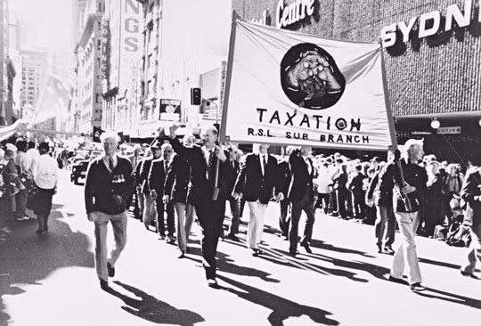 The Taxation RSL sub-branch in the Sydney Branch of the ATO had existed since the 1920s but its members always marched with their service units. In 1995 when Australia celebrated 50 years since the end of World War Two, tax officers raised funds through the sale of Australia Remembers badges. With the money they bought a Taxation RSL sub-branch banner which returned tax officers marched behind in the special parade. The banner shows two hands squeezing blood out of a stone.