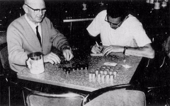 The Melbourne Deputy Commissioner, wearing his grey cardigan, helps count cash collected by tax officers from cars at intersections during the 1965 Miss Taxation competition.